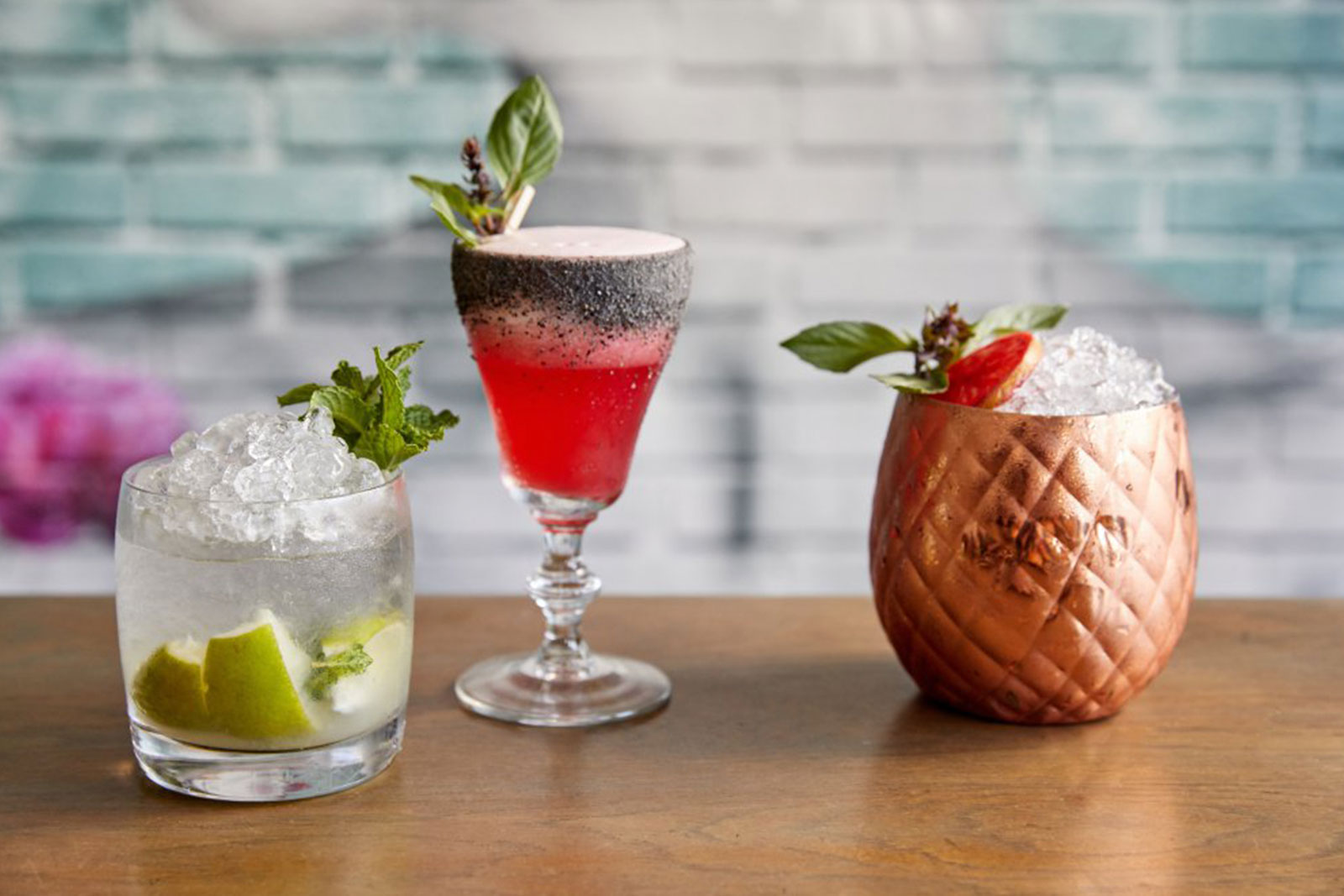 Three Cocktails on a table: gin and tonic, Moscow mule, and a strawberry cocktail with basil